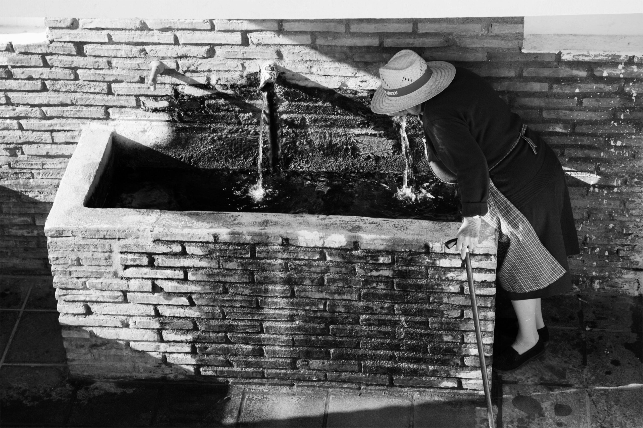 Fuente de rubite en blanco y negro y una señora mayor bebiendo de ella